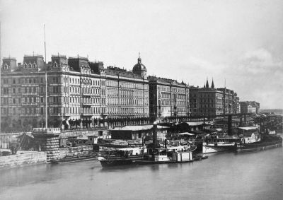A Duna-part (Ferenc J�zsef s�t�ny) a L�nch�dr�l n�zve. Balra a Stein-h�z, m�g�tte a T�zsde, majd a Vigarda (ma: Vigad�) teret hat�rol� Thonet-udvar �s lejjebb a Hung�ria Sz�ll�. A k�p jobb sz�l�n a Belv�ros alacsony h�zai l�tszanak. 1875 k�r�l. Budapesti T�rt�neti M�zeum