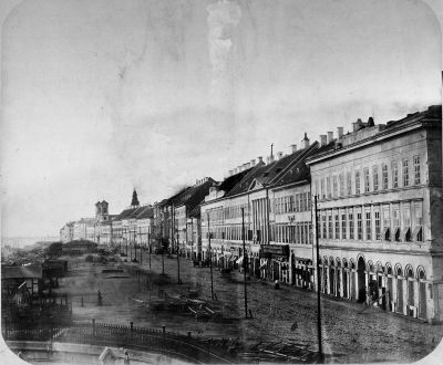 A klasszicista Fels� Duna-sor a L�nch�d t�r fel�l. Balra a Lloyd-palota oldala, a t�volban a g�r�g maced�n templom emelkedik. K�z�tt�k f�l�ton a m�g romos Redut �p�let �s az angol kir�lyn� sz�ll� l�tszanak. A Redut el�tt az egykori haj�h�d h�dv�m h�zik�i �llnak. 1859. Ismeretlen f�nyk�p�sz felv�tele. Magyar Nemzeti M�zeum